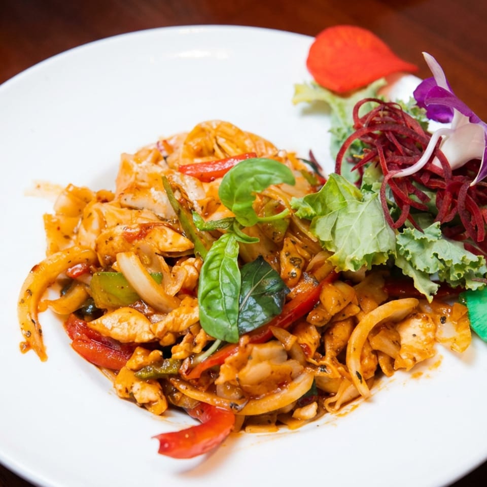 Stir-fried noodles with chicken, vegetables, and basil garnished with leafy greens, shredded beet, edible flowers, and cucumber.