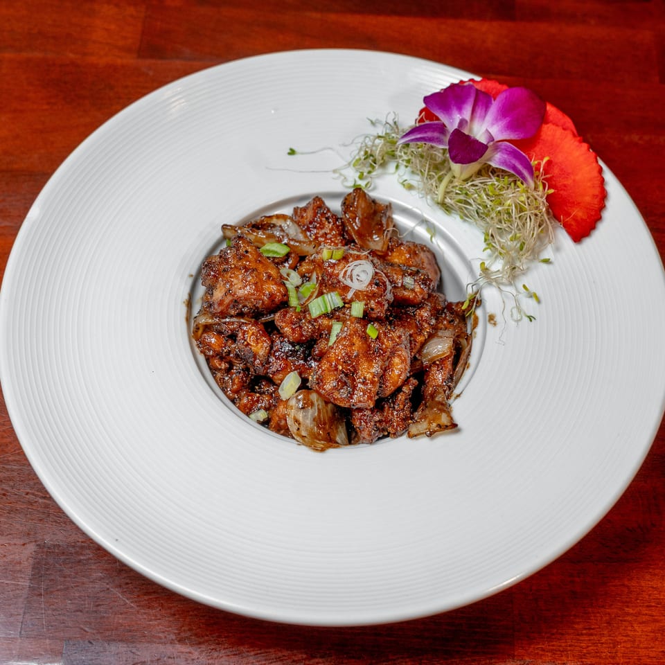 Glazed grilled meat topped with scallions, served with sprouts and orchid garnish on a white plate.