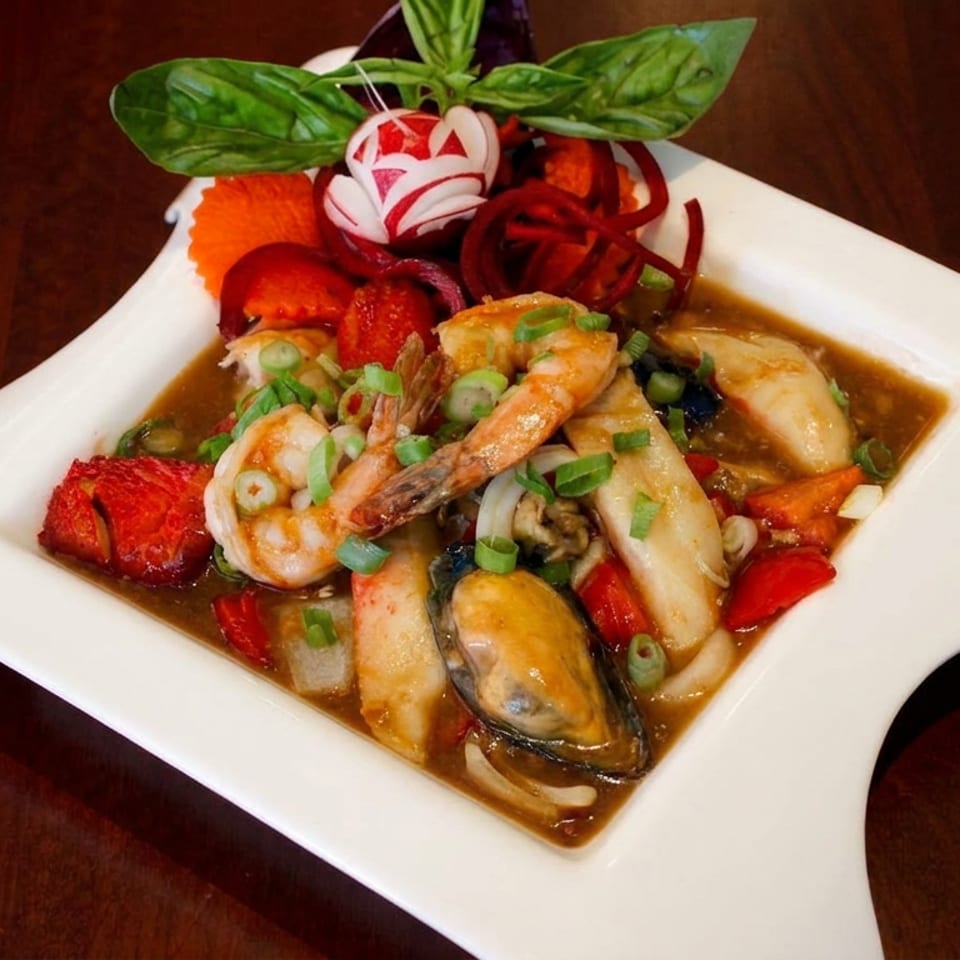 Seafood stir-fry with shrimp, mussels, squid, vegetables, and scallions in brown sauce on a white plate.