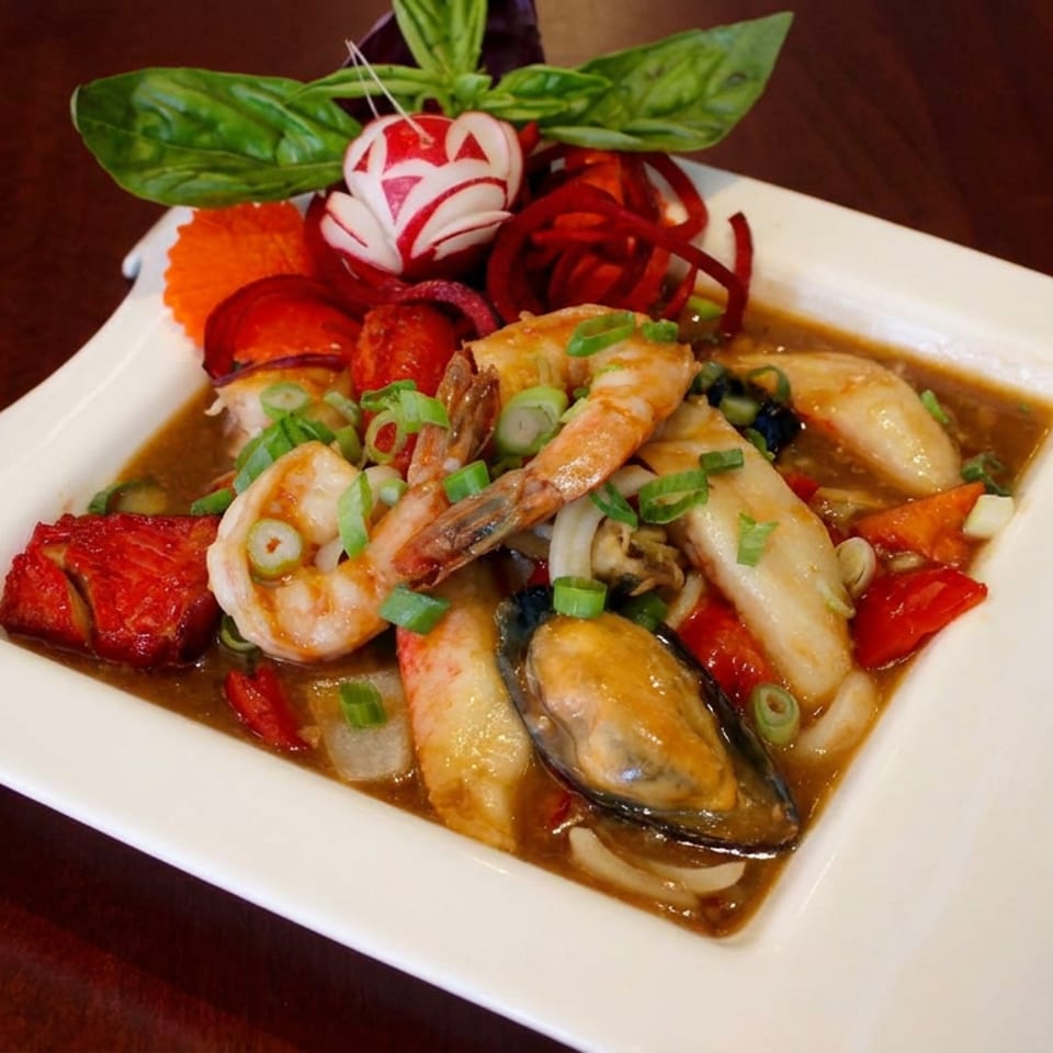 Seafood stir-fry with shrimp, mussels, squid, vegetables, and scallions in brown sauce on a decorative white plate.