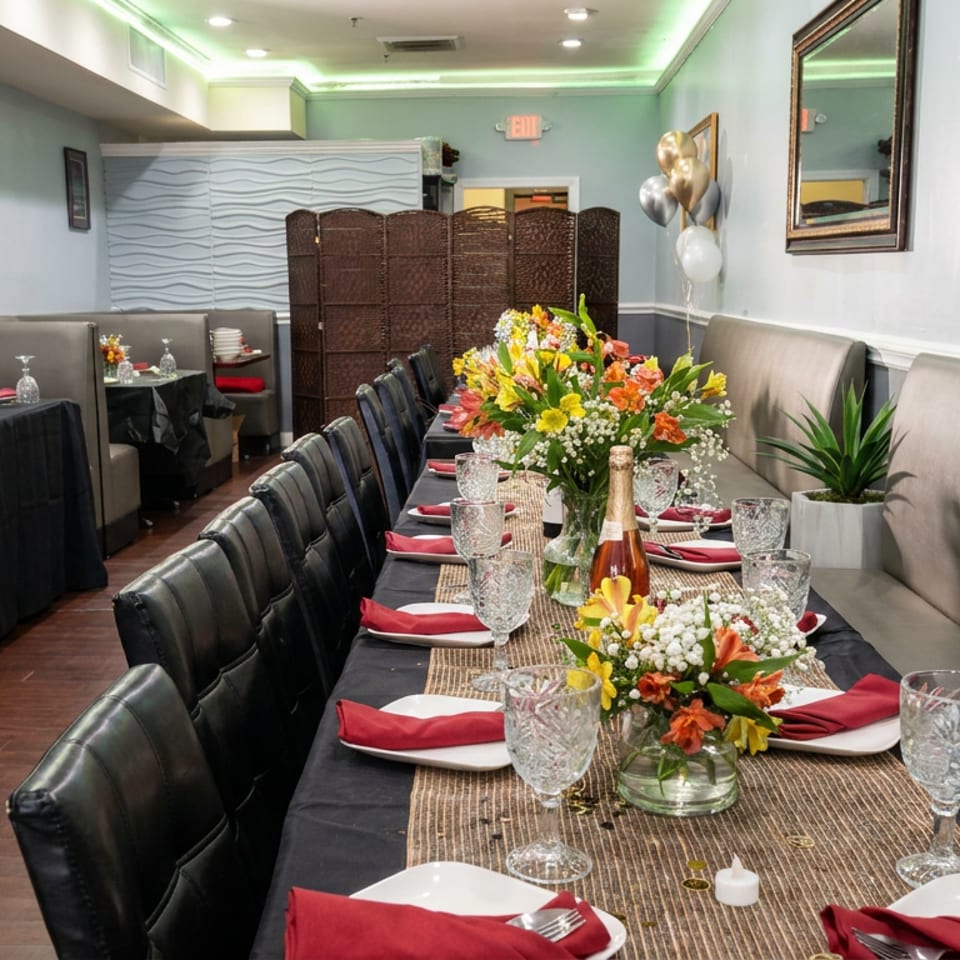 Elegant restaurant dining room with black-clothed tables, floral centerpieces, champagne, red napkins, and upholstered booths.