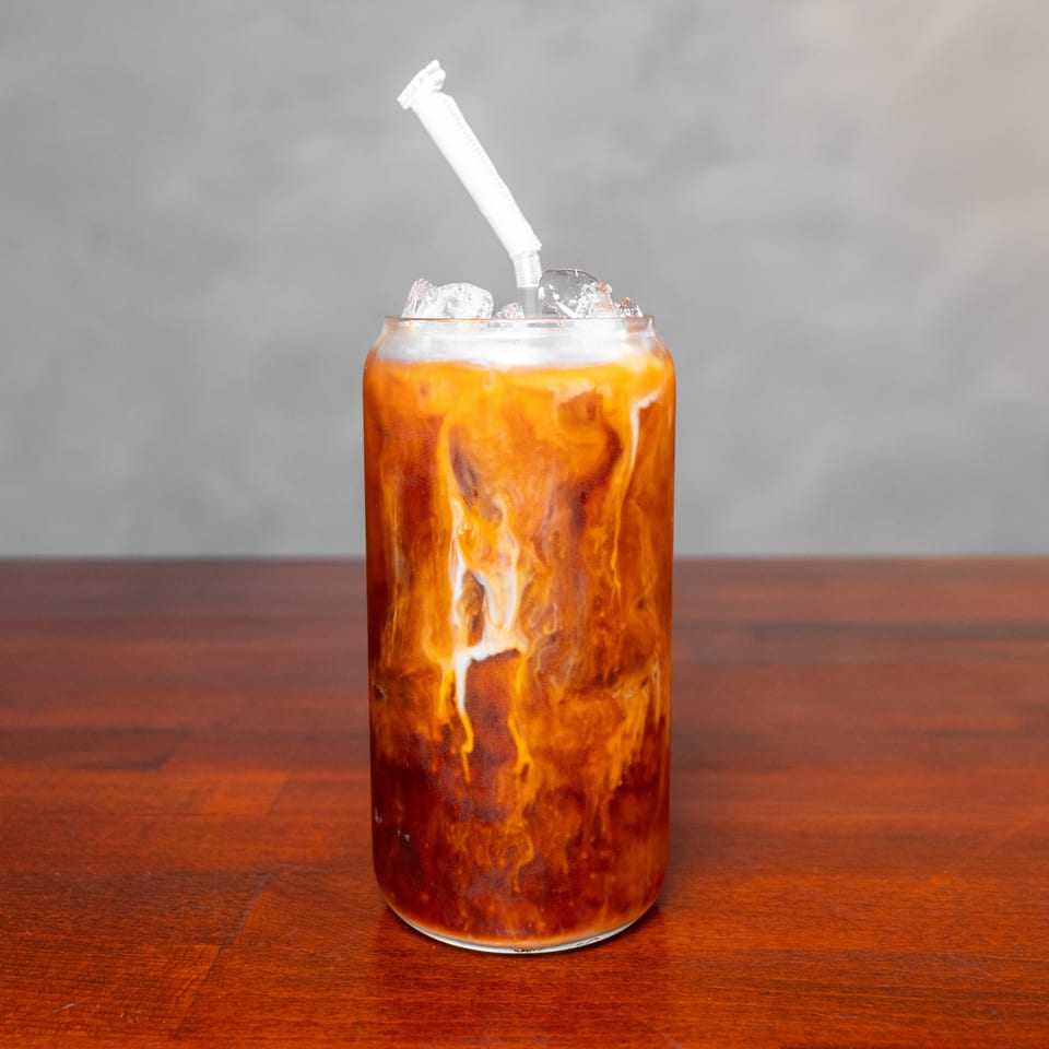 Iced caramel-colored coffee drink with swirling cream, ice cubes, and a straw in a glass on a wooden table.