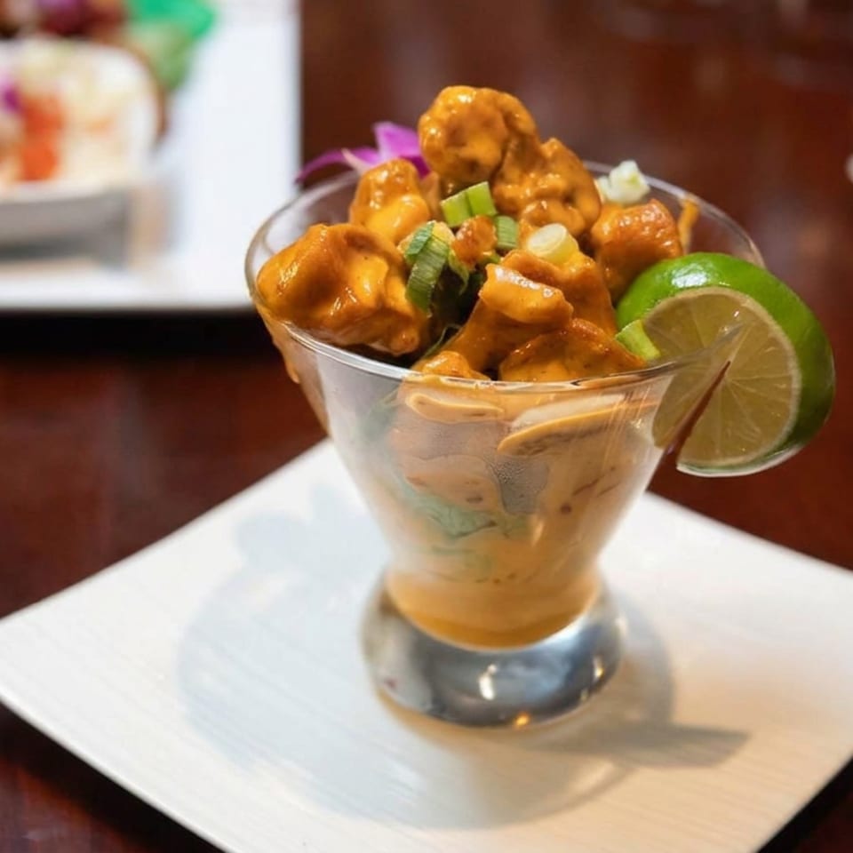 Glazed chicken bites with scallions and lime garnish served in a cocktail glass on a white plate.