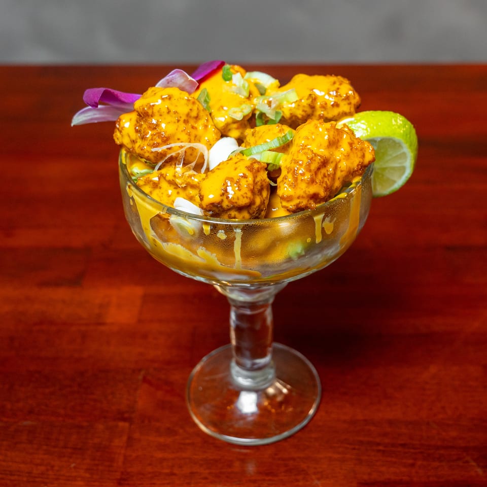 Glazed orange-sauced chicken pieces garnished with scallions and lime in a glass dessert dish on a wooden table.