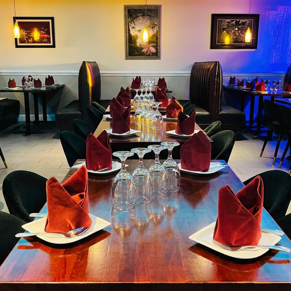Elegant restaurant dining room with red folded napkins, inverted wine glasses, dark seating, framed artwork, and blue ambient lighting.