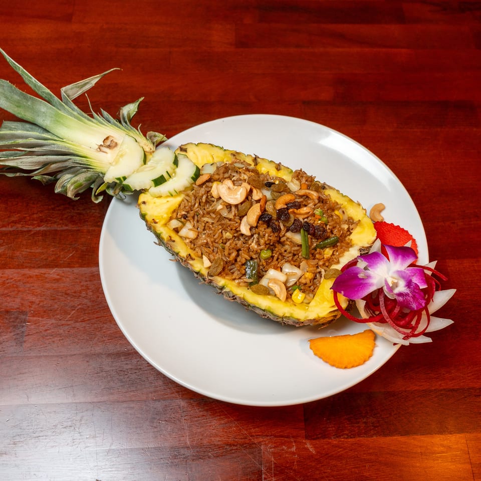 Pineapple fried rice with cashews, raisins, vegetables, cucumber, and edible flowers served on a white plate.