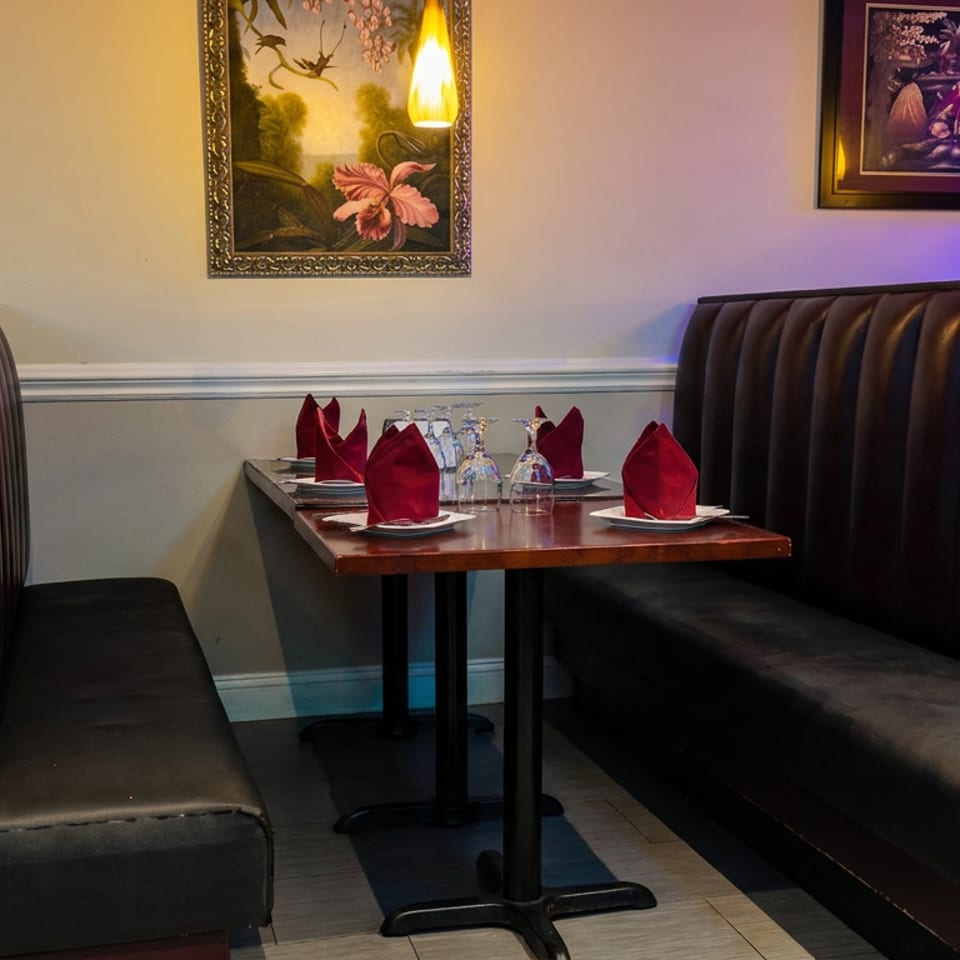 Elegant restaurant booth with dark leather seating, set table, red folded napkins, glassware, floral artwork, and warm pendant lighting.